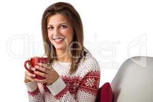 Smiling cute brunette holding cup of coffee sitting on sofa