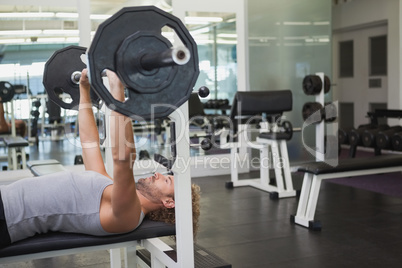 Young muscular man lifting barbell in gym