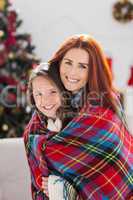 Festive mother and daughter wrapped in blanket