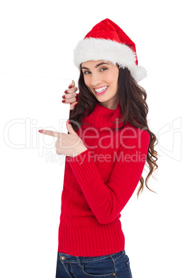 Smiling brunette in santa hat pointing white poster