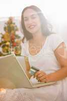 Smiling brunette shopping online with laptop at christmas