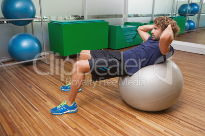 Man doing abdominal crunches on fitness ball in gym