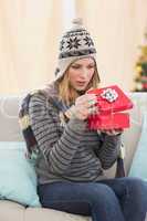 Blond woman opening a gift sitting on a sofa