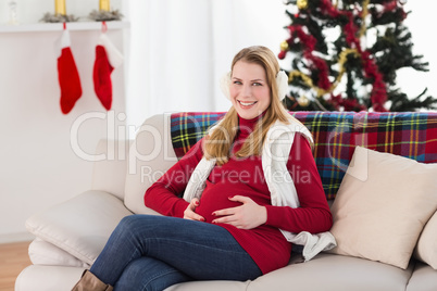 Beautiful pregnant woman holding her belly sitting on couch