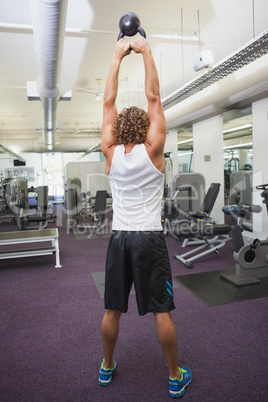 Rear view of man lifting kettle bell in gym