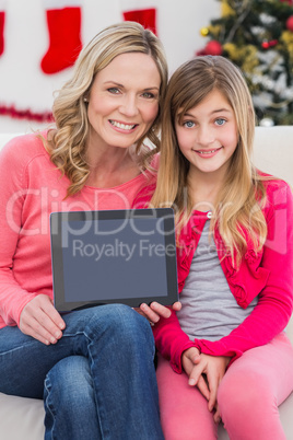 Festive mother and daughter showing tablet screen