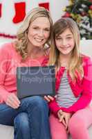Festive mother and daughter showing tablet screen