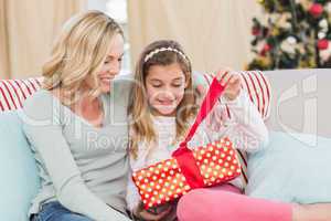 Cute little girl sitting on couch opening gift with mum