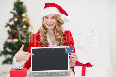 Festive blonde shopping online with laptop and pointing at it