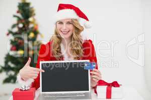 Festive blonde shopping online with laptop and pointing at it