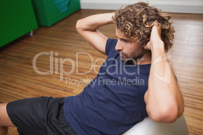 Man doing abdominal crunches on fitness ball in gym