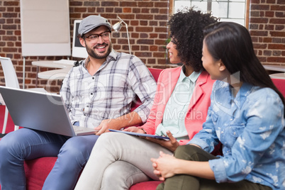 Young casual colleagues using laptop on couch