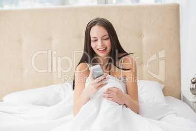 Pretty brunette sending a text on bed