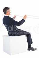 Businessman sitting on a cube and holding rope