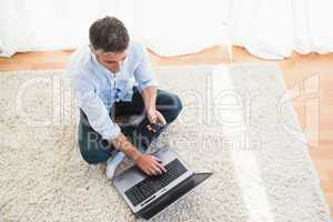 Man sitting on carpet using laptop and phone