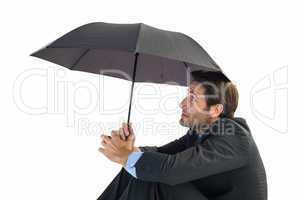 Businessman holding umbrella sitting on the floor