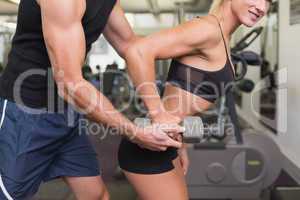 Male trainer assisting woman with dumbbell in gym