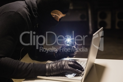 Robber hacking a laptop while making light with his phone