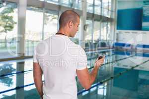 Swimming coach looking at stopwatch by pool at leisure center