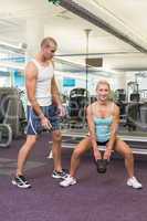 Trainer assisting woman with kettle bell in gym