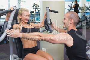 Trainer assisting woman on fitness machine at gym