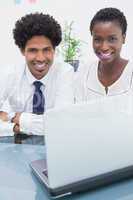 Happy colleagues using laptop and looking at camera