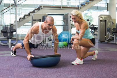 Female trainer assisting man with push ups at gym