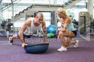 Female trainer assisting man with push ups at gym