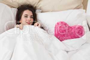 Pretty brunette in bed with heart cushion