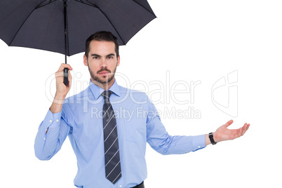 Serious businessman holding umbrella with arm out