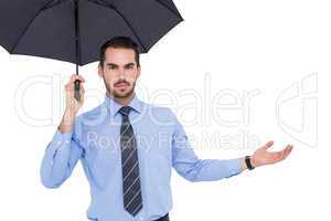 Serious businessman holding umbrella with arm out