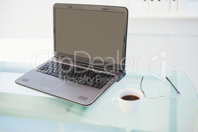 Laptop on desk with mug of coffee and glasses