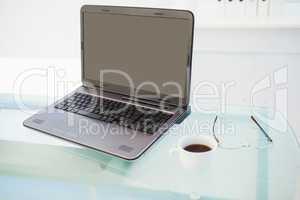 Laptop on desk with mug of coffee and glasses