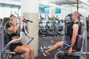 Fit young couple using fitness machines at gym
