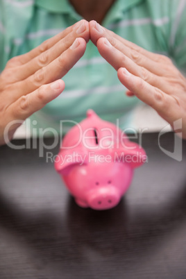 Mans hands sheltering  piggy bank
