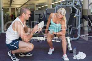 Male trainer assisting woman with dumbbell in gym