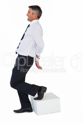 Businessman with one foot on cube and hands behind his back