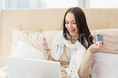 Pretty brunette using laptop on bed to shop online