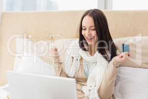 Pretty brunette using laptop on bed to shop online