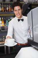 Young barista offering cup of coffee smiling at camera