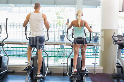 Rear view of couple working on x-trainers at gym