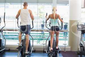 Rear view of couple working on x-trainers at gym