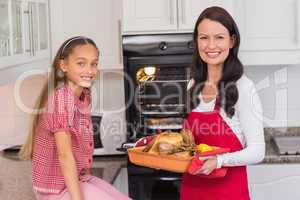 Happy mother and daughter posing with roast turkey