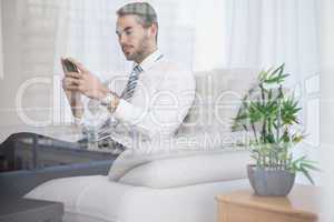 Businessman texting on his couch seen through glass