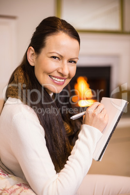 Smiling brunette sitting on the couch writing her christmas list