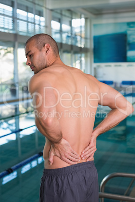 Rear view of shirtless swimmer with back ache by pool