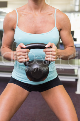 Mid section of a woman lifting kettle bell in gym