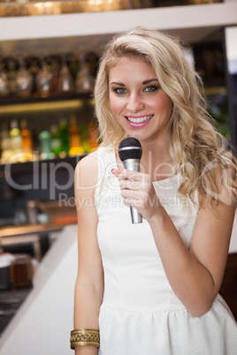 Blonde woman smiling while singing into a microphone