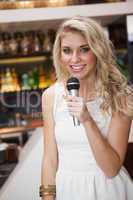 Blonde woman smiling while singing into a microphone