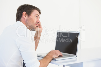 Thinking businessman sitting at desk using laptop